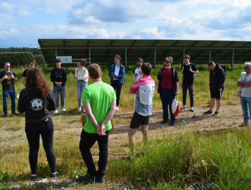 Gesprächsrunde bei der Führung am Solarpark Uttenreuth im Juni 2023 mit der Photovoltaik-Anlage im Hintergrund