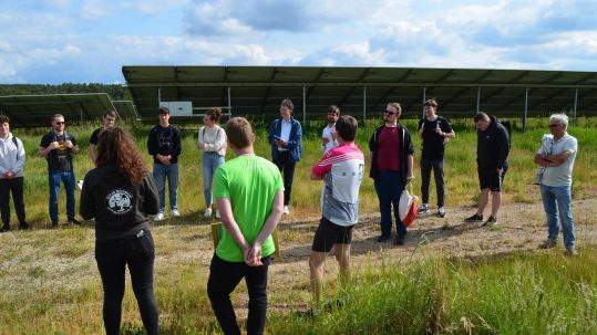 Gesprächsrunde bei der Führung am Solarpark Uttenreuth im Juni 2023 mit der Photovoltaik-Anlage im Hintergrund