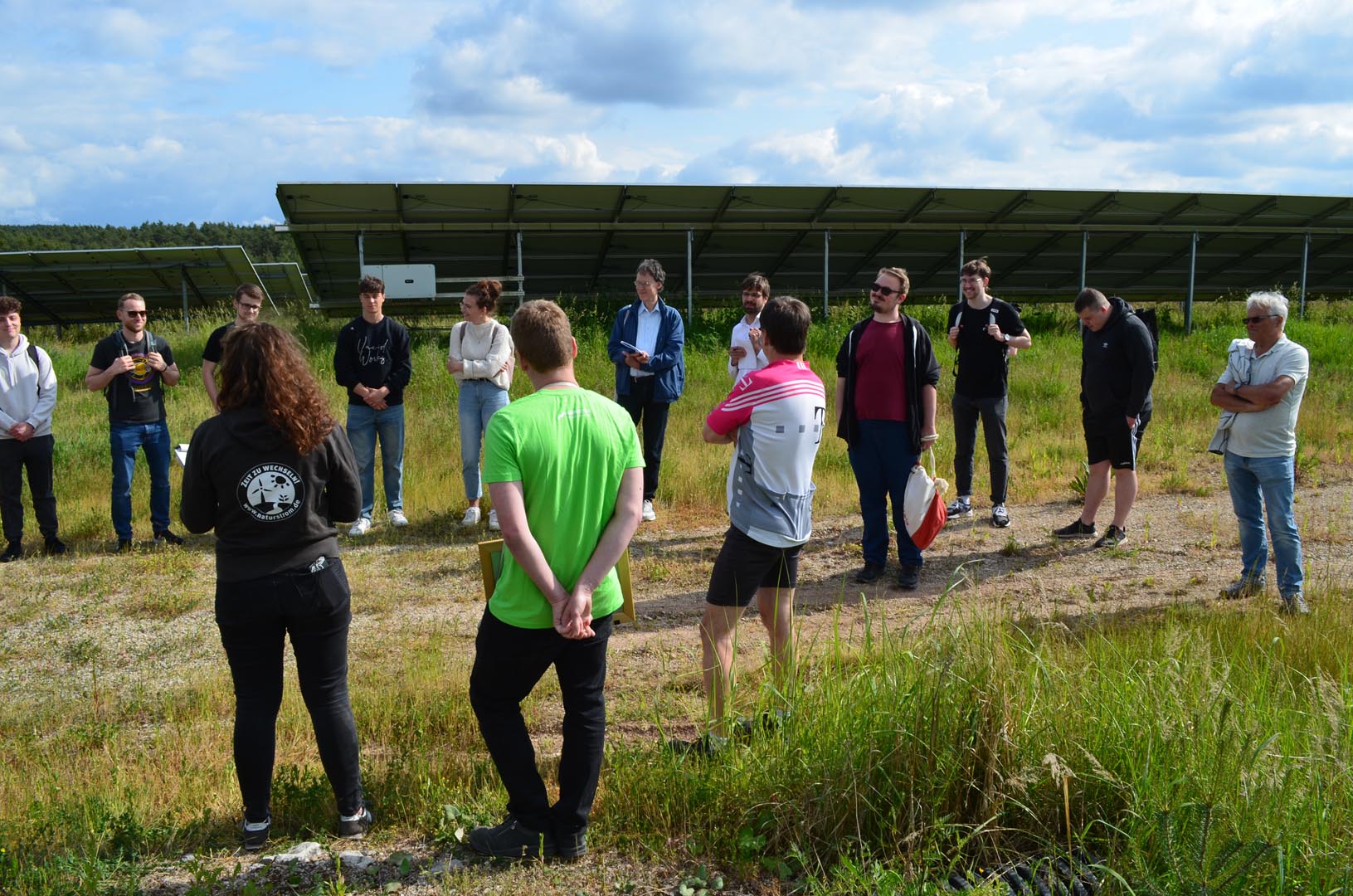 Gesprächsrunde bei der Führung am Solarpark Uttenreuth im Juni 2023 mit der Photovoltaik-Anlage im Hintergrund